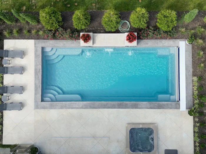 Overhead aerial view of a Thursday Pools Goliath 16x37 fiberglass inground pool in Diamond with an automatic safety cover, 12-jet square spa, 14-foot water feature wall, and concrete patio.