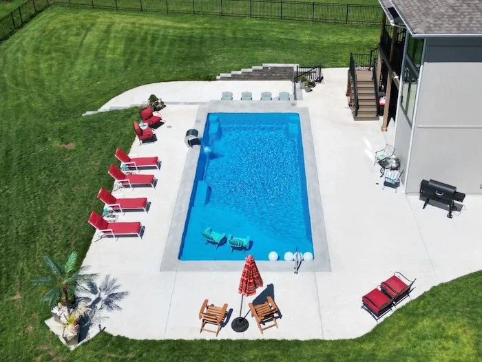 Wide aerial view of a Thursday Pools Aspen 16x35 fiberglass inground pool in California Blue with an expansive concrete entertaining patio, installed by Tiger Pool and Patio, one of Kansas City's premier pool contractors.