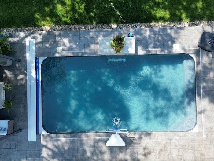 Overhead drone view of a Kansas City inground pool by Tiger Pool and Patio featuring 18x36 pool with a Merlin Shelter Cove vinyl liner, full-width bench with corner steps, diving board, and premium patio pavers.