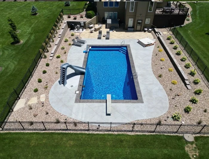 Professional vinyl liner pool builder Tiger Pool and Patio completes 18x40 Diver pool in Kansas City with GLI Cayman Mystic Light Blue liner, granite left turn Typhoon slide, integrated deck jets, and ergonomic step and bench combination.