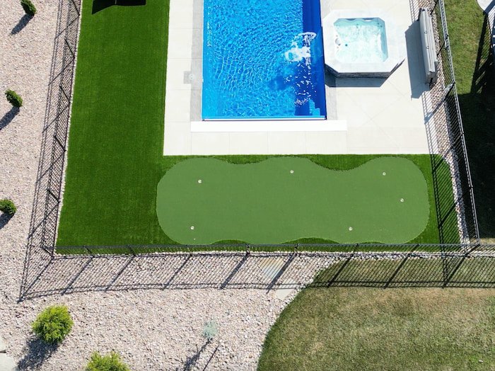 Aerial close-up of a backyard putting green and Cardinal fiberglass spillover spa adjacent to a Thursday Pools Aspen 16x40 in Maya Blue, a unique backyard pool and patio feature by Tiger Pool and Patio.
