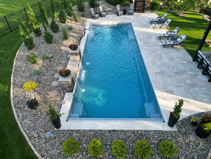 Ground-level view of a Thursday Pools Goliath 16x41 fiberglass inground pool in Diamond with a cascading water feature wall, travertine pavers, and professional landscaping.