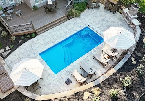 Tiger Pool and Patio fiberglass inground pool installation in Kansas City—Thursday Pools Aspen 12x25 in California Blue with paver patio, coping stones, and outdoor fireplace.