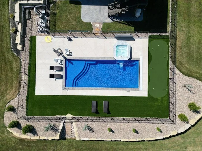 Full aerial view of a Kansas City backyard pool and patio by Tiger Pool and Patio—Thursday Pools Aspen 16x40 in Maya Blue with automatic safety cover, Cardinal spillover spa, putting green, and turf border surround.