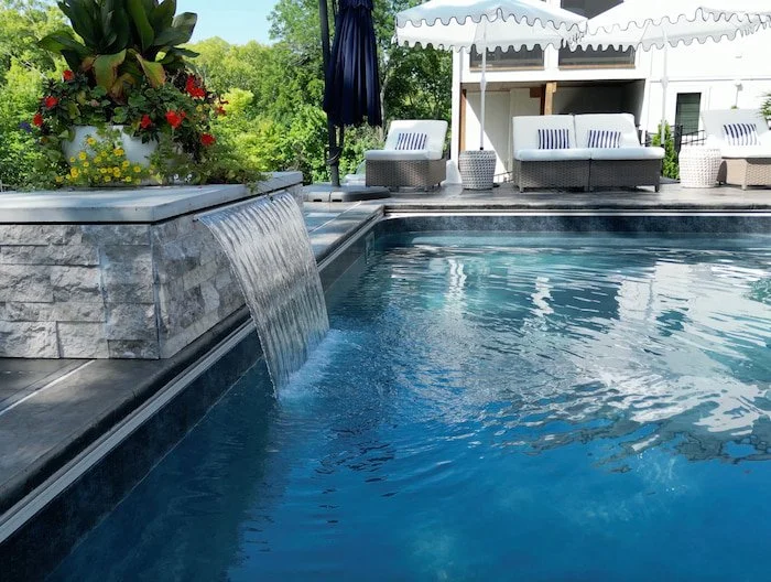 Complete backyard pool and patio design showing 18x36 fiberglass pool with a Merlin Shelter Cove vinyl liner, 3-foot water feature wall, and custom outdoor living space.