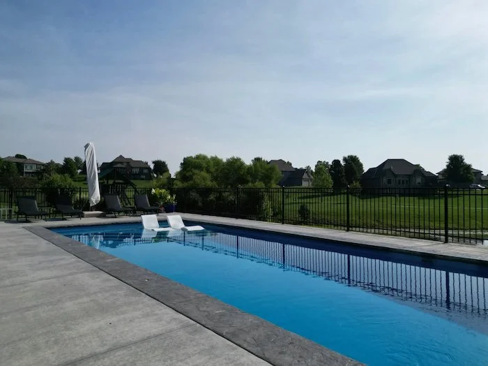 Ground-level view of a Thursday Pools Aspen 16x40 fiberglass inground pool in California Blue with tanning ledge chairs and decorative coping, set against an open Kansas City backyard.
