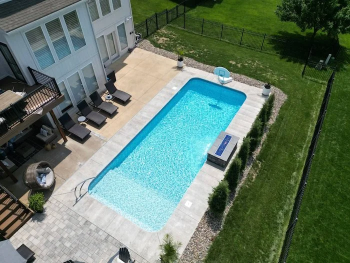 A 14x30 vinyl liner inground pool with Serene Tile and Honey Pearl Floor liner, featuring a full-length sun deck, fire and water feature wall with blue fire glass, and a basketball hoop in the shallow end.