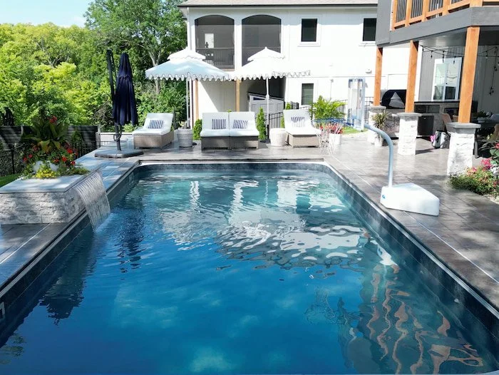 Complete Kansas City pool installation by Tiger Pool and Patio showing 18x36 a fiberglass pool with Merlin Shelter Cove liner, stone water feature wall, automatic safety cover, and outdoor living space with a cabana.