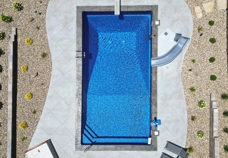Aerial view of an 18x40 vinyl liner inground pool with diving board, water slide, and deck jets installed by Tiger Pool and Patio.