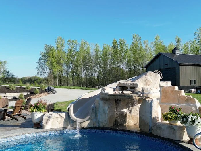 Rico Rock faux rock slide and waterfall feature built into a 20x42 custom lagoon vinyl liner pool with Opal Bay liner, with a curved slide, cascading waterfall, and flower pot accents.