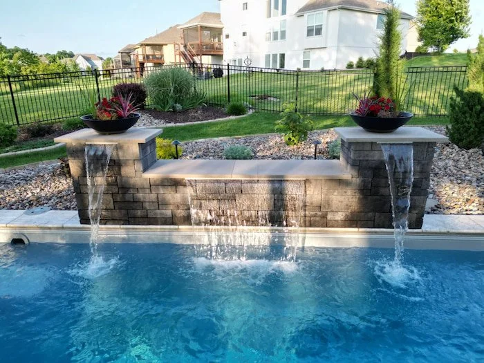 Close-up of a custom 12-foot water feature wall cascading into a fiberglass inground pool, a signature design element of this Kansas City pool project.