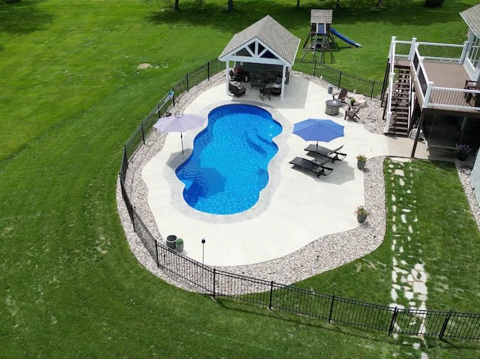 Tiger Pool and Patio fiberglass pool installation featuring the Thursday Pools Sun Day 16x39 in Maya color, with a pool house pavilion, children's play set, and black aluminum fence in a Kansas City backyard.