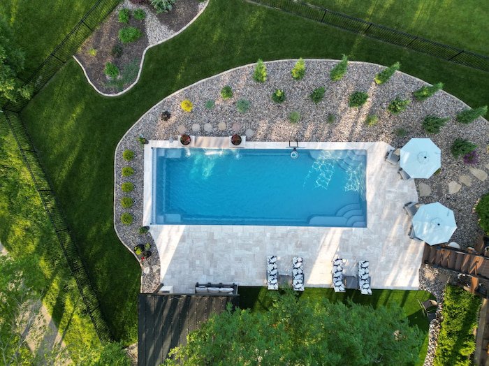 High aerial view of a Tiger Pool and Patio fiberglass inground pool installation in Kansas City—Thursday Pools Goliath 16x41 in Diamond surrounded by travertine pavers, rock landscaping, and a manicured lawn.