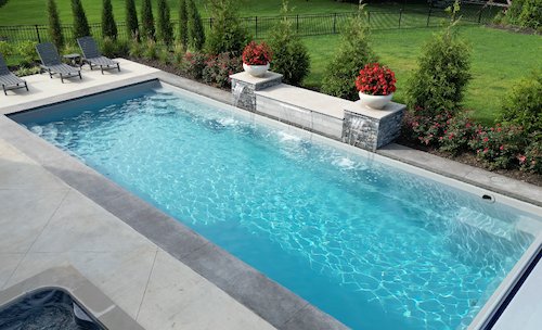 Tiger Pool and Patio fiberglass inground pool installation—Thursday Pools Goliath 16x37 in Diamond with a 14-foot water feature wall, square spa, and travertine paver surround.