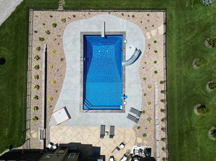 Tiger Pool and Patio Kansas City pool contractor installation of a 18x40 Diver vinyl liner pool with a GLI Cayman Mystic Light Blue finish, granite Typhoon slide, deck jets, diving board, step and bench combo, and landscaped patio areas.