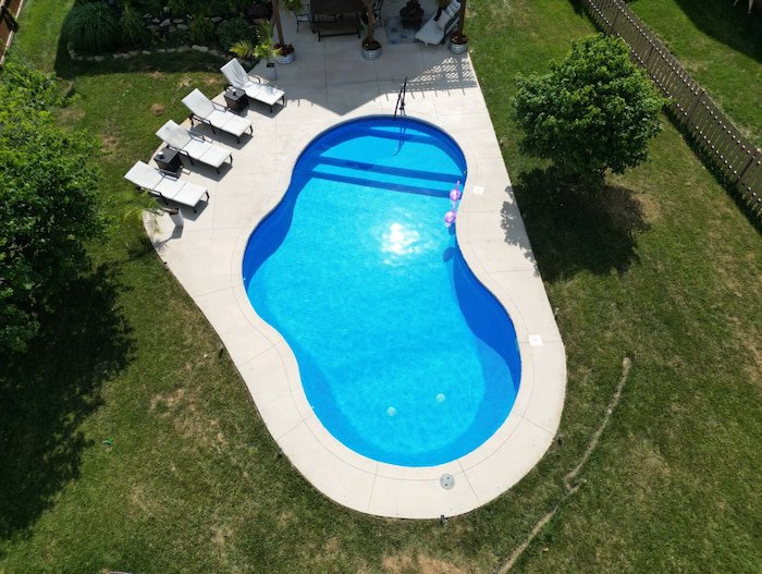 Aerial view of professional vinyl liner pool installation in Kansas City showing Merlin Blue Quartz finish on a Mountain Lake fiberglass inground pool design with an integrated sun deck.