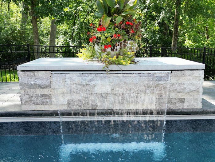 Tiger Pool and Patio installation featuring a 3-foot natural stone water feature wall with sheet waterfalls and decorative planter on a 18x36 inground pool remodel with a Merlin Shelter Cove liner.