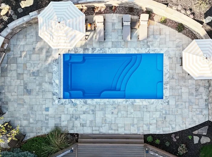 Kansas City backyard pool and patio by Tiger Pool and Patio featuring a Thursday Pools Aspen 12x25 fiberglass pool with Belgard paver surround, stone retaining wall, and outdoor fireplace.