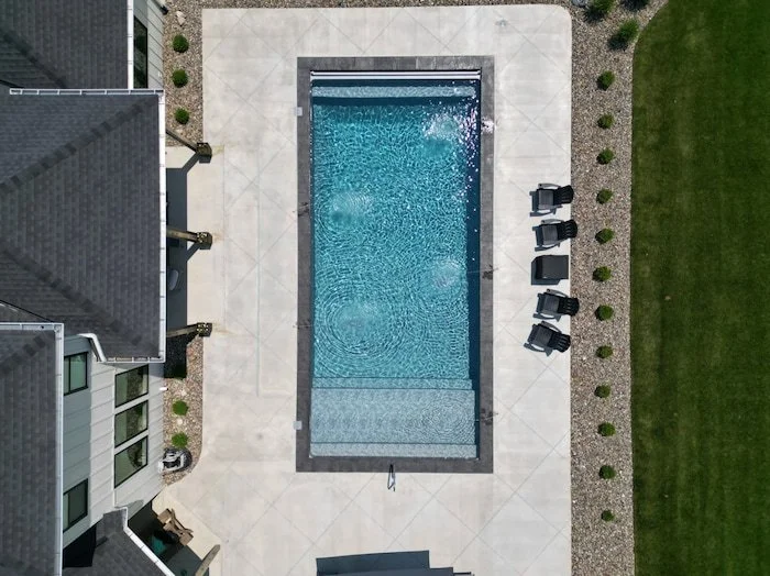 Overhead drone view of a Tiger Pool and Patio 20x40 inground vinyl liner pool in Island Granite with slate coping, 6-inch radius corners, a tanning ledge, and an automatic safety cover with a stone lid.