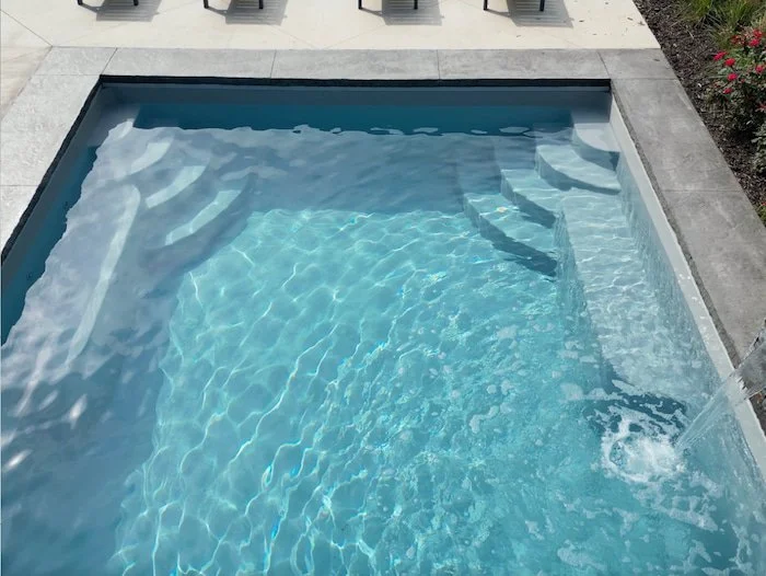 Close-up of the crystal-clear interior of a Thursday Pools Goliath 16x37 fiberglass inground pool in Diamond, showing the tanning ledge and entry steps.
