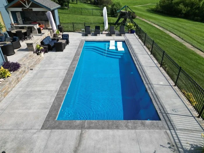  Thursday Pools Aspen 16x40 fiberglass inground pool in California Blue with tanning ledge chairs and decorative coping, installed by Tiger Pool and Patio alongside a Kansas City pool house and outdoor kitchen.