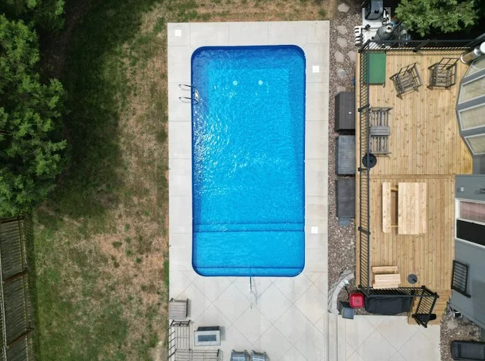 A 16x32 vinyl liner pool installation with a stunning Jamaica floor pattern creating tropical aesthetic, expansive full-length sun deck maximizing shallow-end enjoyment for families, artisan handrails providing safe pool access, geometric concrete pa