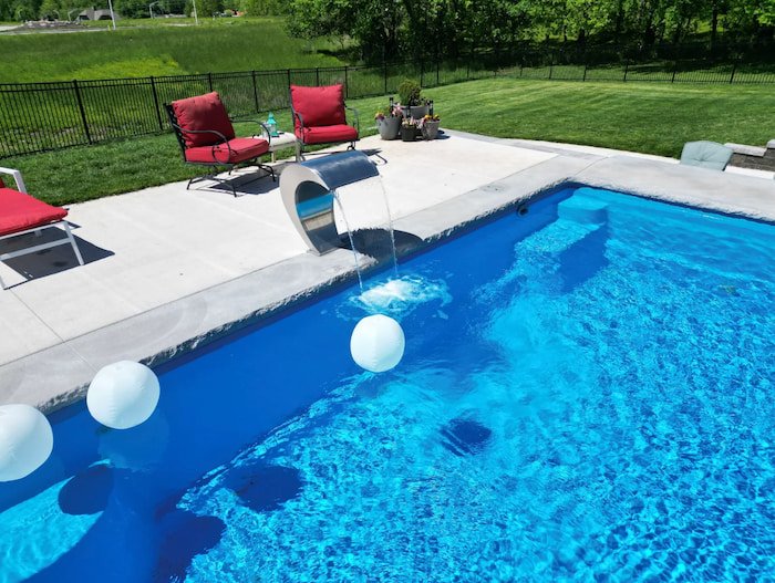 Close-up of the Grand Effects Escala stainless steel waterfall cascading into a Thursday Pools Aspen 16x35 fiberglass inground pool in California Blue.