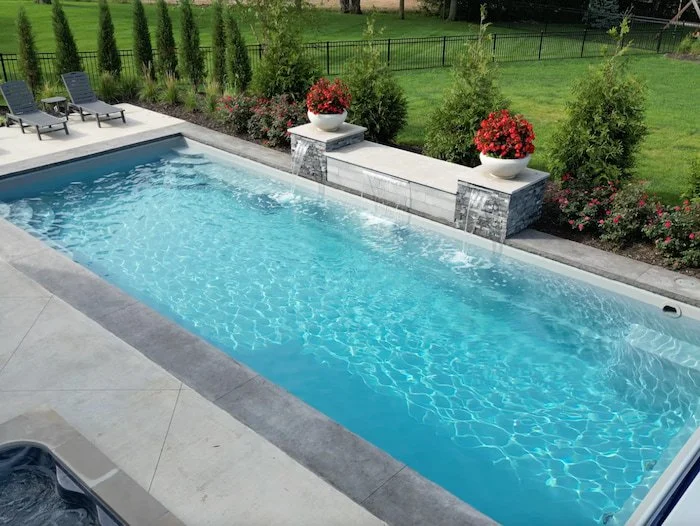 Ground-level view of a Thursday Pools Goliath 16x37 fiberglass inground pool in Diamond with a cascading water feature wall, travertine paver surround, and lush landscaping, installed by Tiger Pool and Patio in Kansas City.