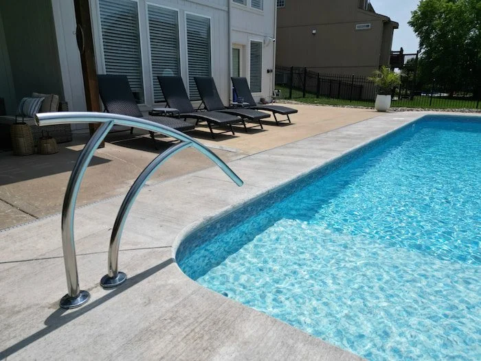 Close-up of the sculptural stainless steel artisan handrail at the full-length sun deck entry of a 14x30 vinyl liner pool with a Serene Tile liner, installed by Tiger Pool and Patio.