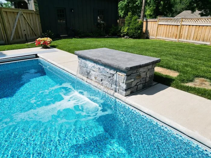 Close-up of the 4-foot stacked ledge stone water feature wall with bluestone cap cascading into a 10x20 personal plunge pool with an Azure Mosaic Borderless liner, installed by Tiger Pool and Patio.