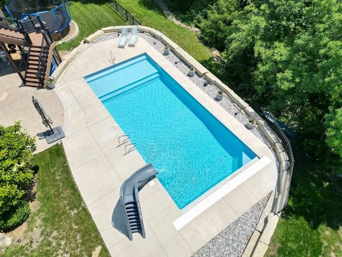 A Kansas City backyard transformation by Tiger Pool and Patio featuring a 18x40 vinyl liner inground pool with a brilliant Mystic Light Blue GLI Cayman finish, automatic safety cover for year-round protection, full-length sun deck with corner bench, 