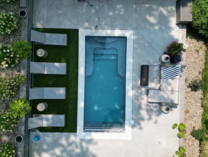 Direct overhead aerial view of a Thursday Pools Sea Turtle fiberglass pool in Diamond with an automatic safety cover, ice coping, turf sun lounger section, and concrete patio.