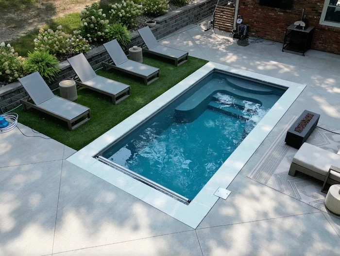 A Thursday Pools Sea Turtle fiberglass inground pool in Diamond with an automatic safety cover, ice coping stones, artificial turf, and a fire pit seating area.