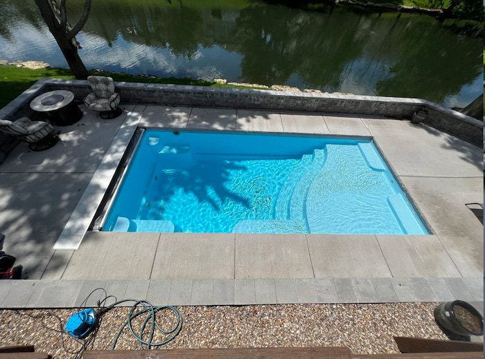 Thursday Pools Aspen 12x25 fiberglass inground pool in Caribbean Sparkle color with large stone retaining walls and a concrete pool deck.