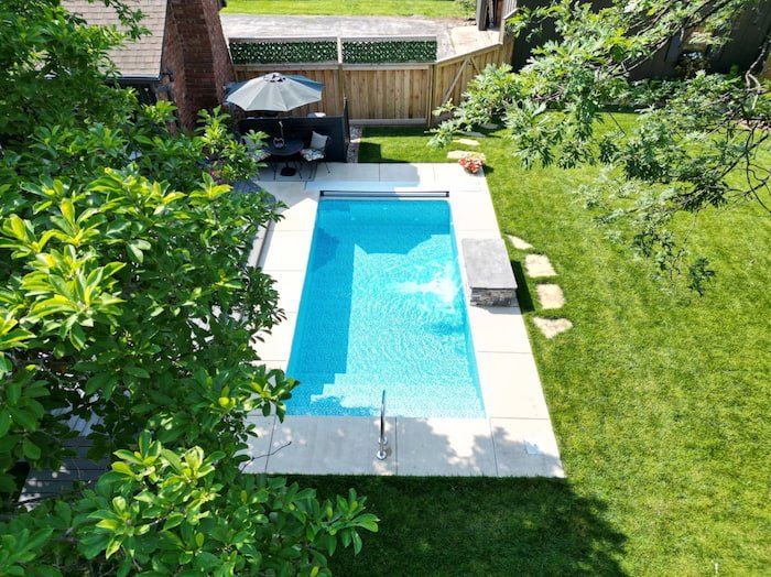 Aerial view of a Tiger Pool and Patio Recreational 10x20 personal plunge pool with an Azure Mosaic Borderless liner and automatic safety cover, tucked into a compact Kansas City backyard with a concrete surround, stainless steel entry rail, and patio