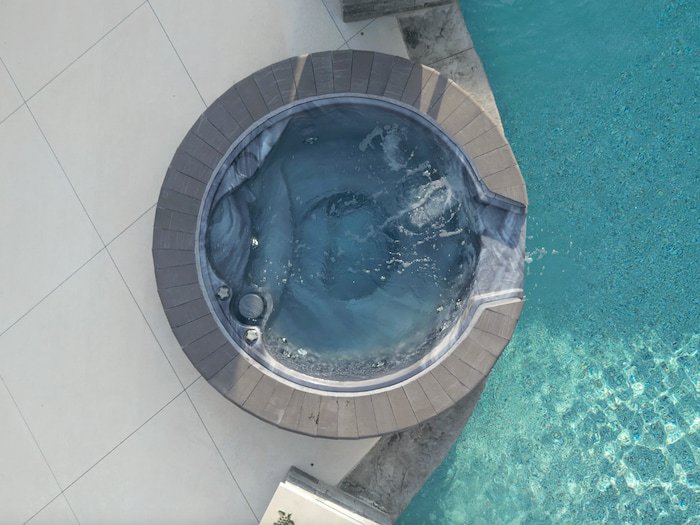A round 12-jet spillover spa with a circular stacked brick coping surround actively bubbling and cascading into a 20x42 custom lagoon vinyl liner pool with a Merlin Beachside Tile and Gold Coast Floor liner.