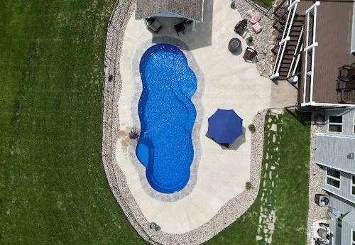 Aerial view of a freeform fiberglass inground pool with sun deck bubblers and decorative coping installed by Tiger Pool and Patio—Thursday Pools Sun Day 16x39 in Maya Blue.