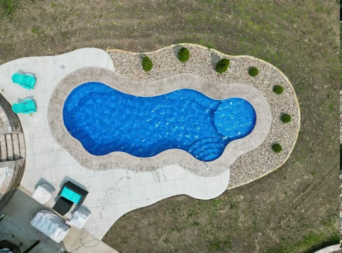 Aerial view of a Thursday Pools Wellspring 16x40 freeform fiberglass inground pool in Maya Blue with a 3-foot coping band, bubblers, and rock border landscaping. 