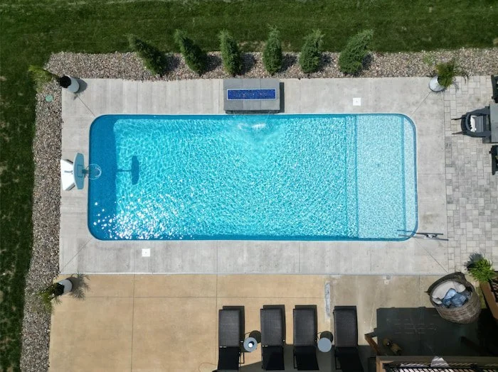 Top-down aerial view of a Tiger Pool and Patio 14x30 vinyl liner inground pool with Serene Tile and Honey Pearl Floor liner, showcasing a full-length sun deck with artisan handrail, 4-foot fire and water feature wall, and concrete pool deck with rive