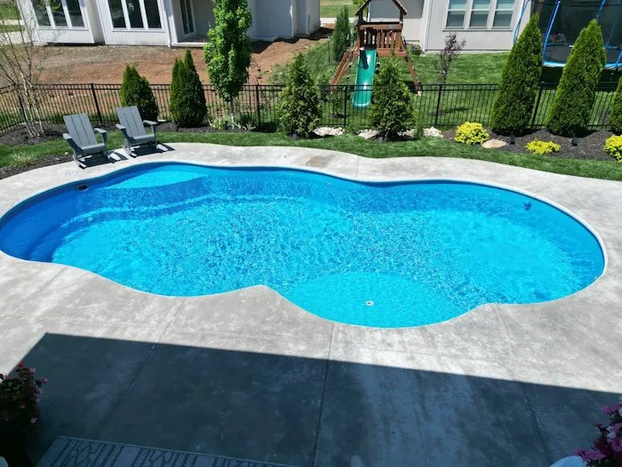 A Thursday Pools Sun Day 15x30 freeform fiberglass inground pool in California Blue with sun deck bubblers and concrete surround, installed by Tiger Pool and Patio in a family-friendly Kansas City backyard.