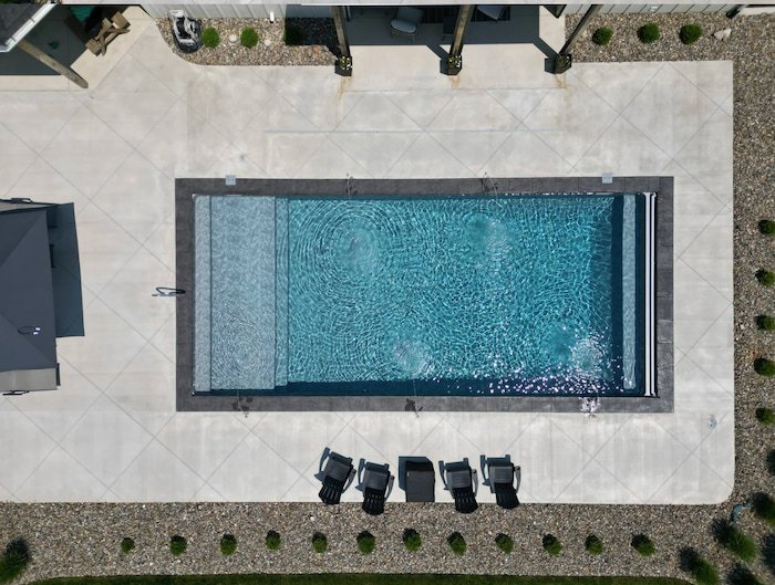 Top-down aerial view of a 20x40 Island Granite vinyl liner pool with five active deck jets, a tanning ledge, 6-inch radius corners, slate coping, and an automatic safety cover with a stone lid.