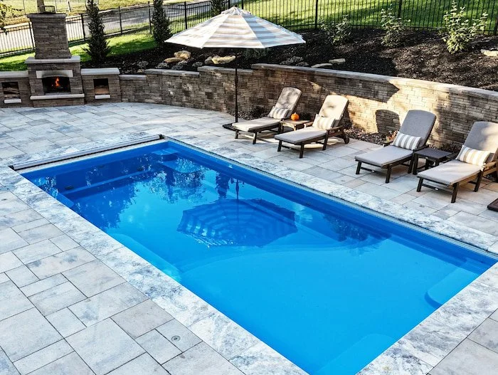 A close overhead view of a Thursday Pools Aspen 12x25 fiberglass pool interior in California Blue with silver tumbled coping and travertine paver surround, installed by Tiger Pool and Patio in Kansas City.