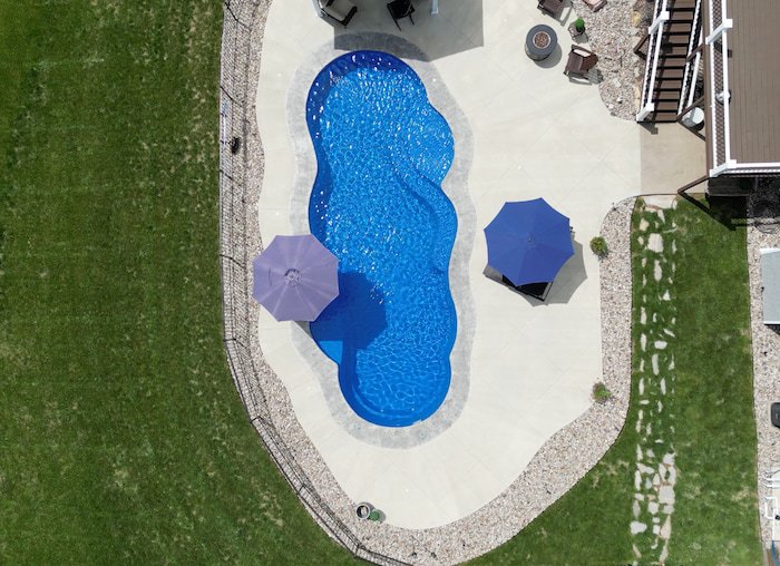 Bird's-eye view of a Thursday Pools Sun Day 16x39 inground fiberglass pool with sun deck bubblers, a river rock landscaping border, and a stamped concrete pool deck.