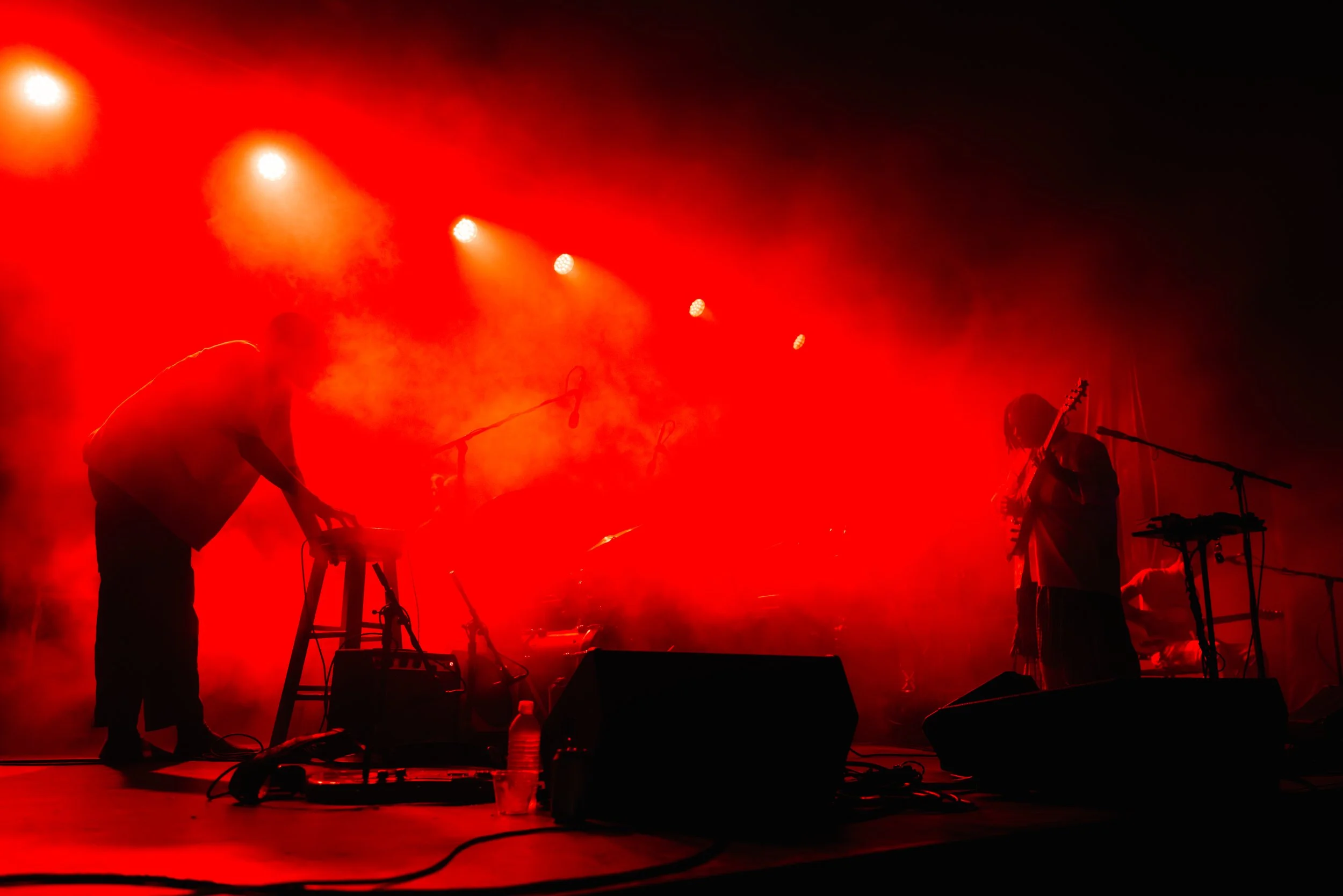 Performers on stage bathed in red light, playing instruments and moving with dynamic lighting effects.