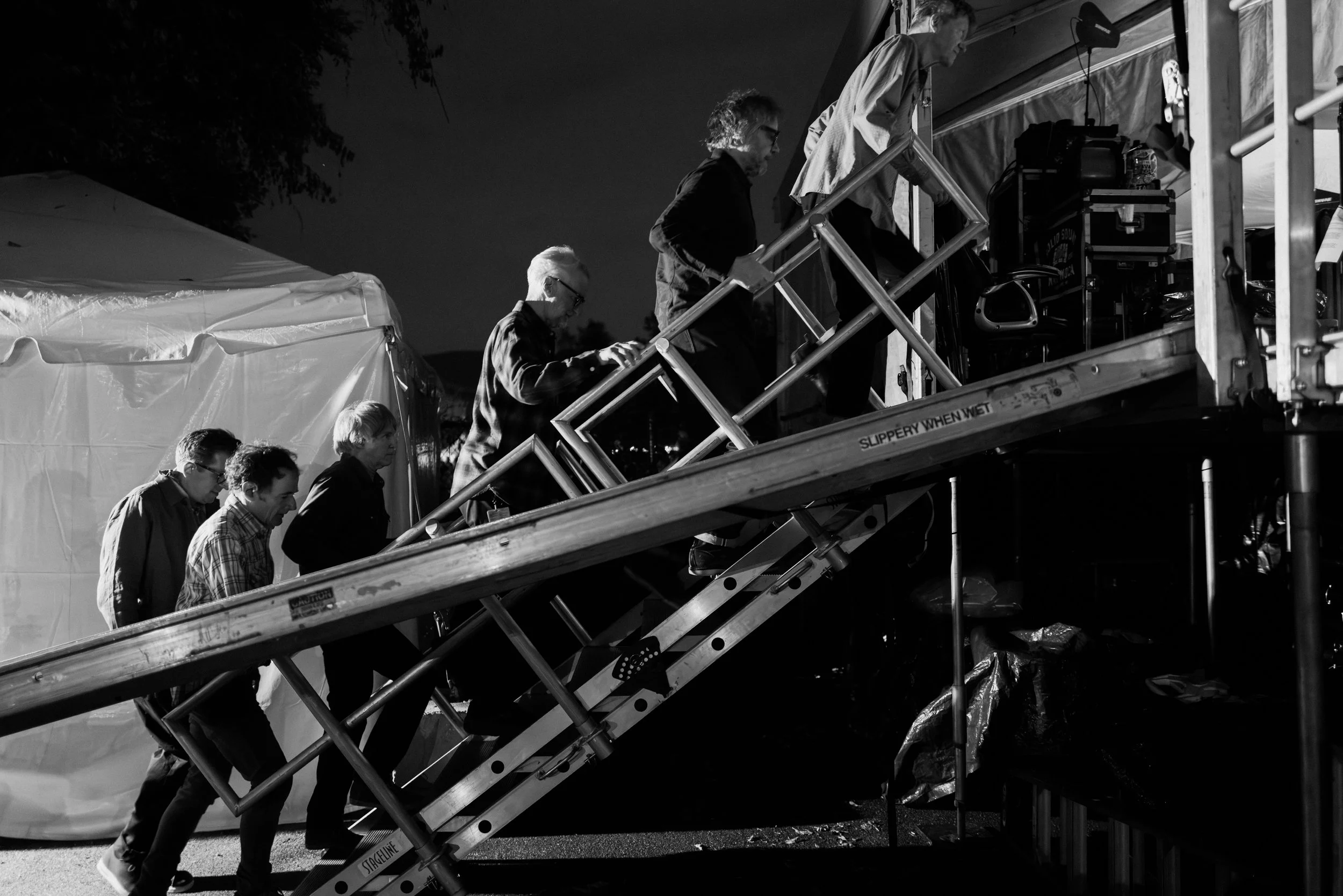 A group of people ascending an outdoor staircase at night, with equipment visible near a building or stage area.