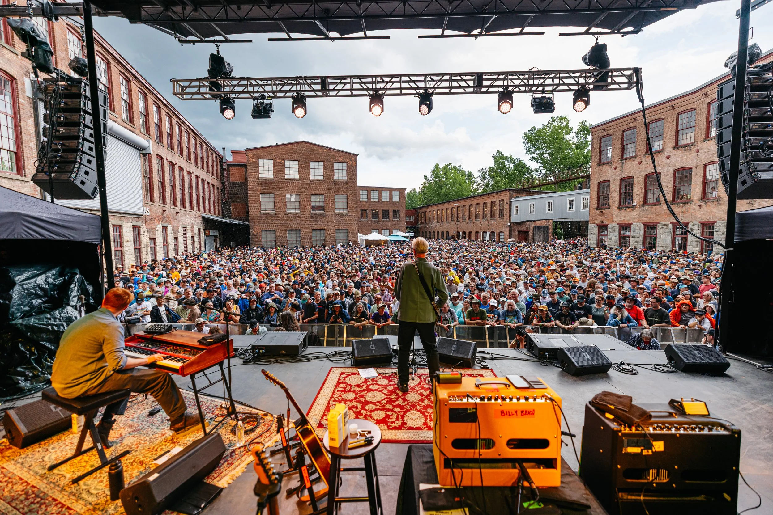 View of an outdoor concert stage with musicians and crowd in an urban industrial setting on a cloudy day. Billy Bragg on stage at Solid Sound 2026.