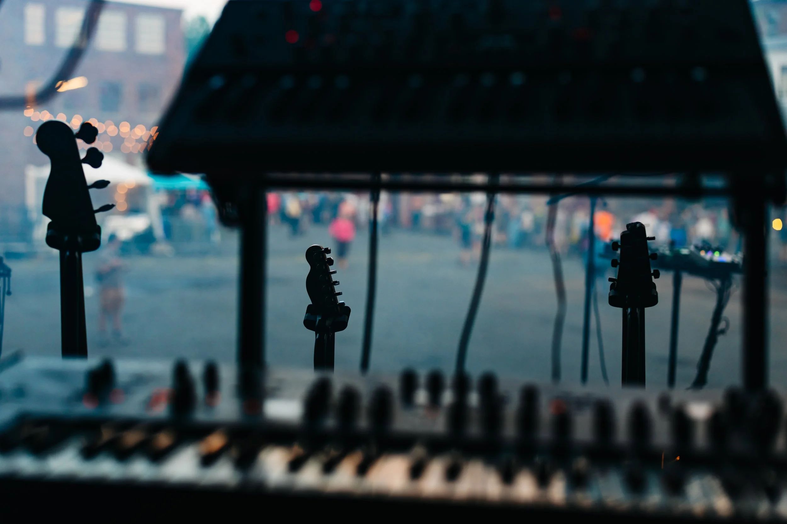 The image shows the view of a city street from inside a vehicle, possibly a bus or train, with blurred pedestrians and vehicles outside, taken through a window. The foreground includes the silhouette of musical instrument headstocks, likely guitars, 
