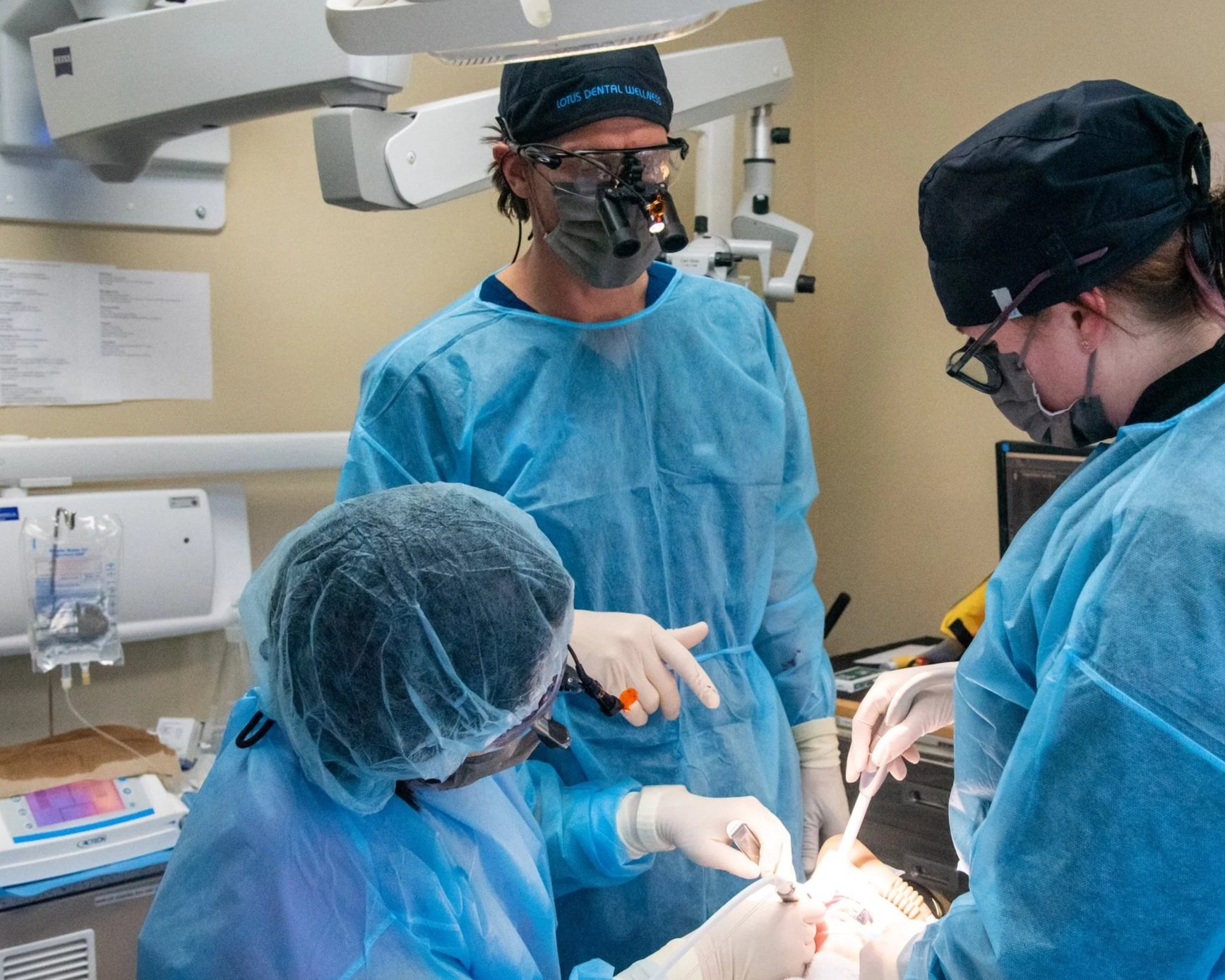 Dr. Shepard DeLong mentoring Dr. Jeeyoung Han during oral surgery wearing blue scrubs and masks in an operating room.