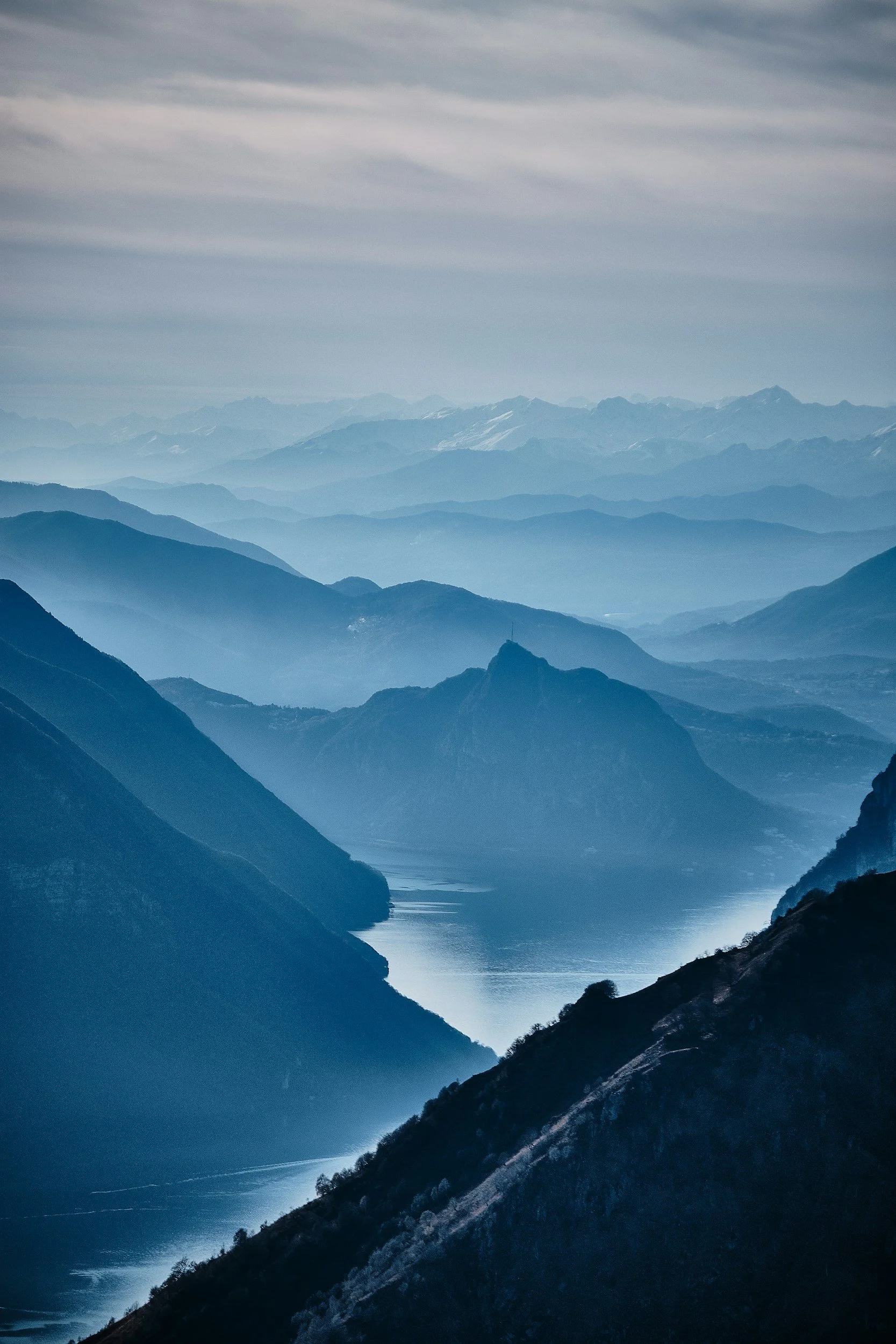 Scenic view of a mountain range with rolling hills and a body of water in the valley, under a cloudy sky.