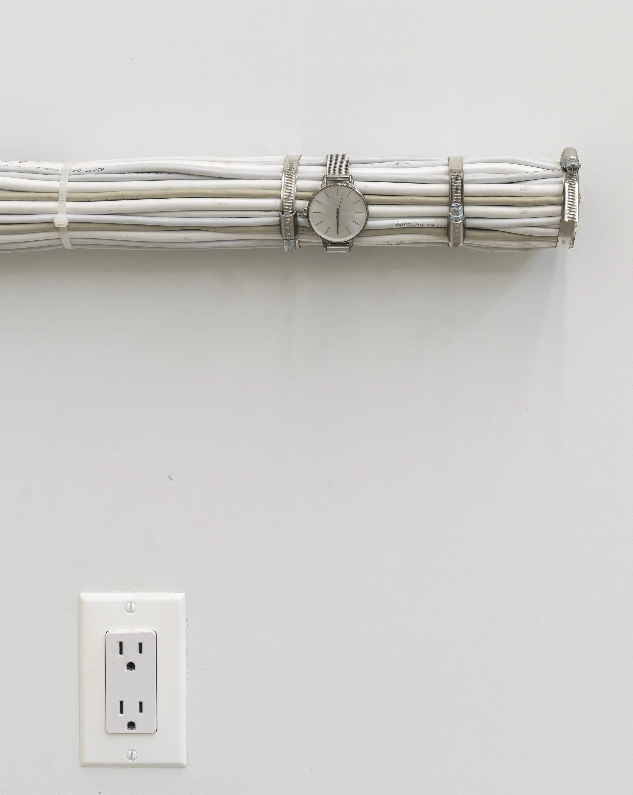 Detail of Rodrigo Red Sandoval’s installation “Time Line” (2025), exhibited at Swivel Gallery in New York. Two wristwatches are strapped onto a long bundle of white data cables, alongside carved segments that reveal the colourful internal wiring.
